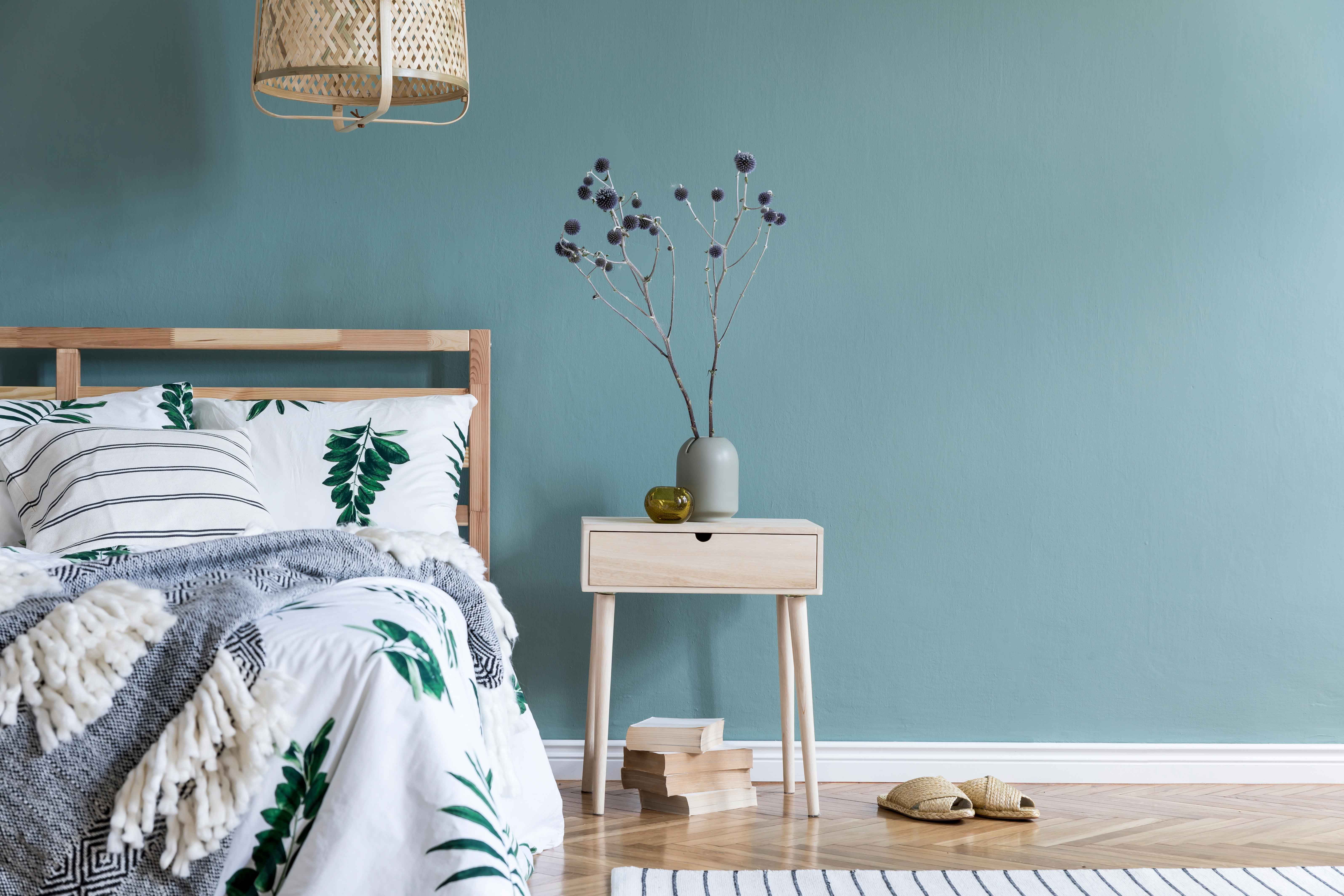 Composición minimalista del interior de un dormitorio con cama de madera, estante, flores en un jarrón, lámpara de ratán, libros y elegantes accesorios